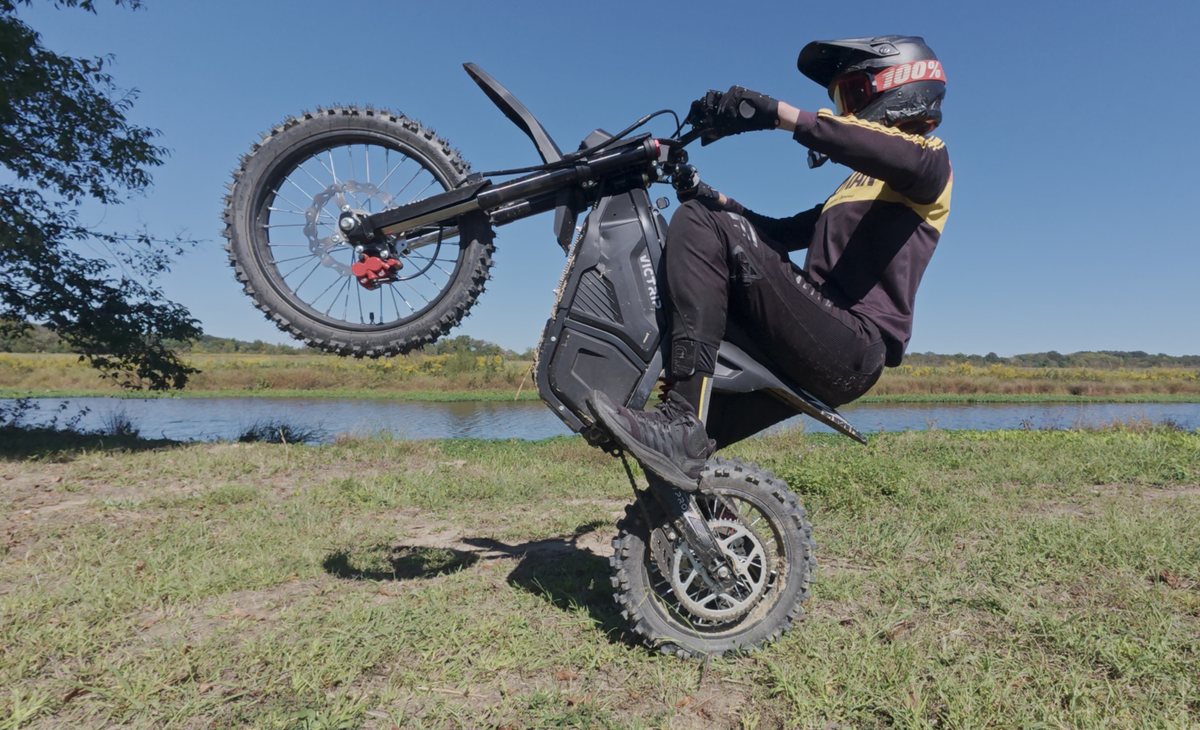 Rider performing a wheelie on an electric dirt bike during an off-road ride